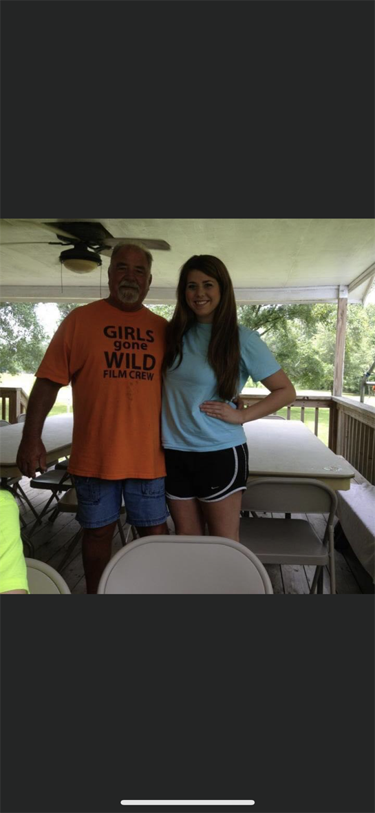 Two friends pose for a picture while enjoying a sunny day in a backyard during a family gathering.