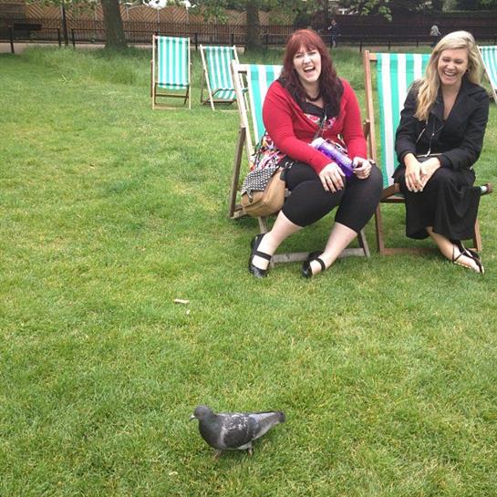 Two women relax on deck chairs, enjoying the sun and each other's company as a pigeon strolls by.