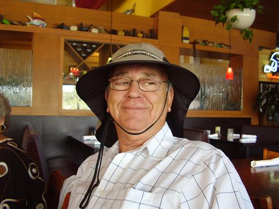 Elderly man smiles broadly while seated in a warm restaurant, enjoying his meal and company.