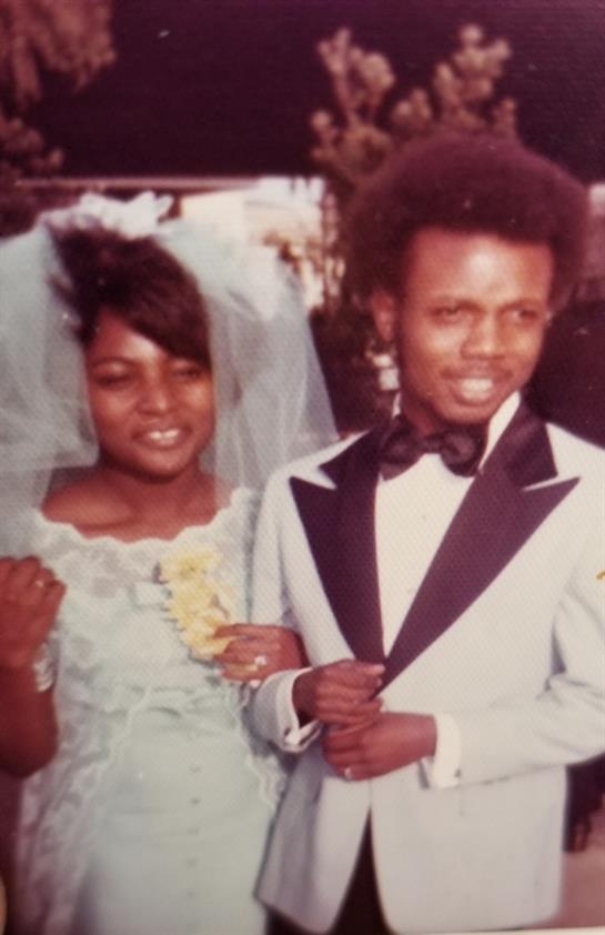 Joyful couple dressed in formal attire, holding each other and smiling on their special day.