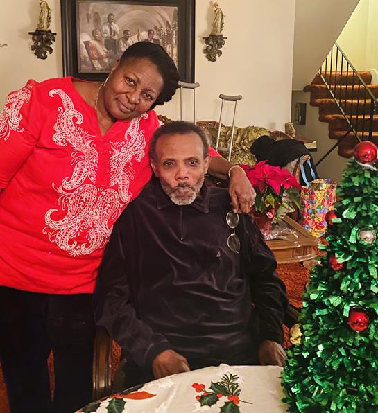 Two family members enjoy a warm gathering near a decorated Christmas tree and festive table.