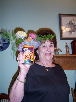 A woman smiles, holding a flower-adorned can of beans at a gathering.