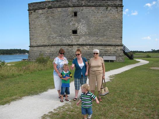 Group of adults and children enjoying a day at a historic site, with a stone fort in the background.