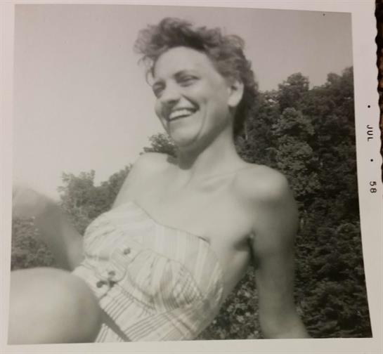A woman in a light dress laughs joyfully, surrounded by greenery during a sunny day.