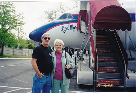 A man and woman stand smiling beside an old airplane, showcasing their joy at the airport.