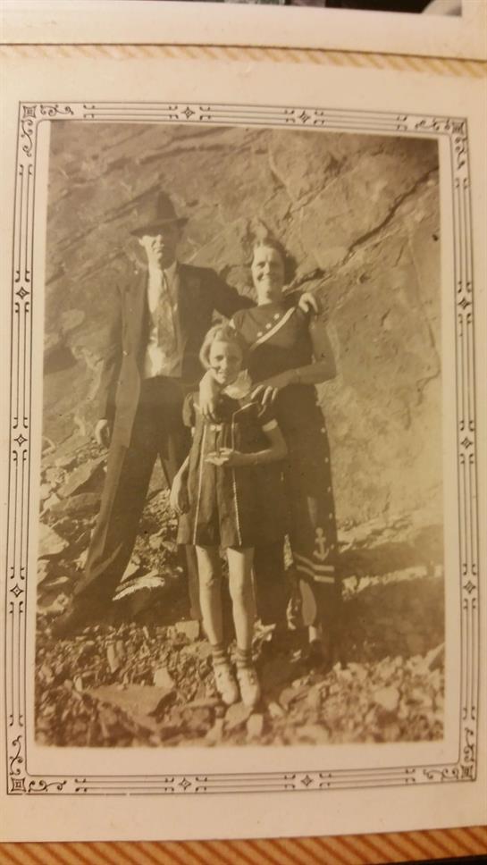 A family poses together outdoors in a sunlit area surrounded by rocks, dressed in vintage clothing.