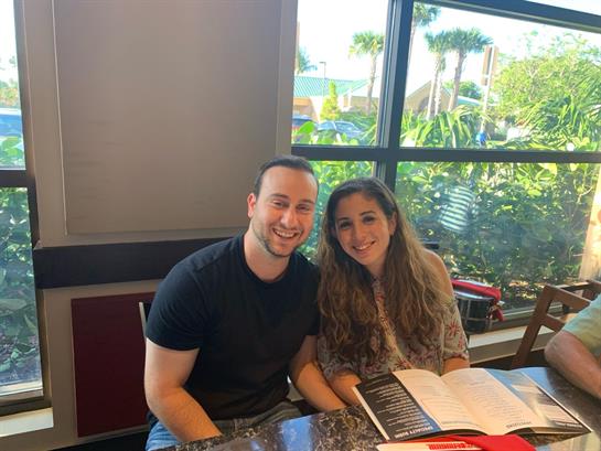 A young couple smiles together while reviewing the menu indoors on a bright day.