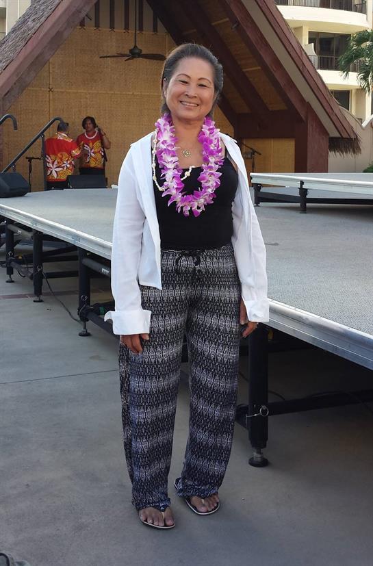 A woman enjoys a cultural celebration wearing a floral lei and relaxed outfit, standing on stage.