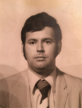 A man in a suit poses for a formal headshot with a serious expression.