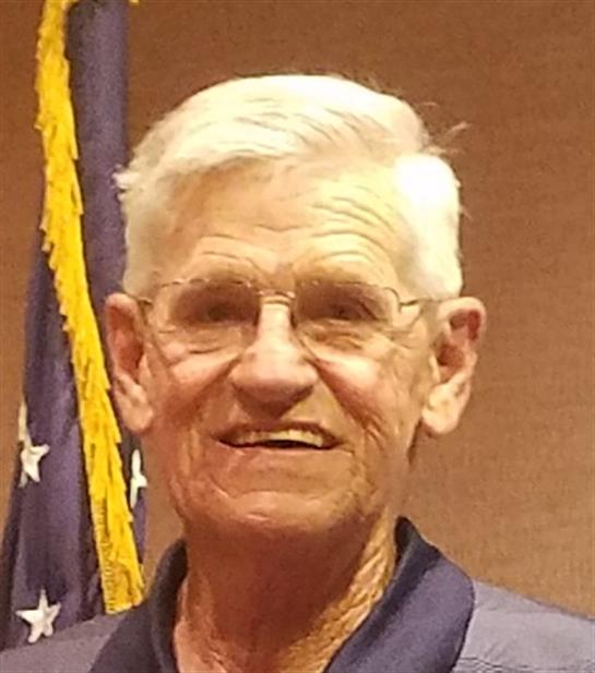 Elderly man smiles broadly while standing beside an American flag during a community gathering.