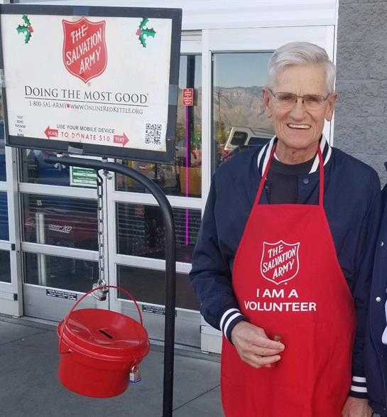 Cheerful senior volunteer engages shoppers while ringing a donation bell for charity.