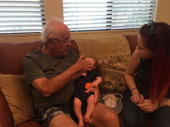 Grandfather feeds his grandchild while the mother watches, creating a cozy family moment.