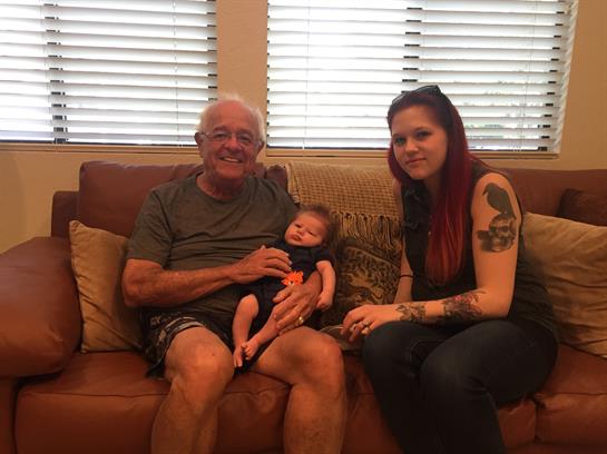 A loving grandfather holds his grandchild while the mother sits beside them, all smiling warmly.