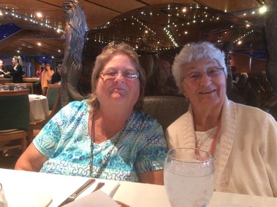 Two women enjoy a meal together in a warm restaurant atmosphere filled with twinkling lights.