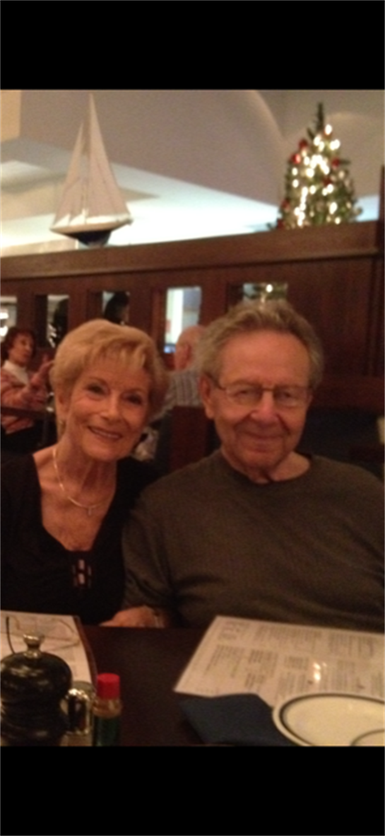 A couple smiles while seated in a busy restaurant, surrounded by friends and cheerful ambiance.
