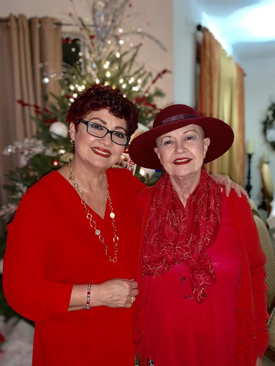 Two women smile happily while dressed in red, surrounded by holiday decorations and warm ambiance.