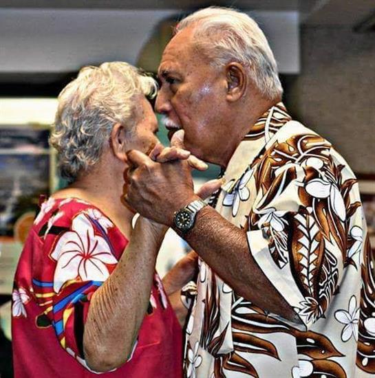 An elderly couple shares a joyful dance in a lively gathering, surrounded by colorful decorations.