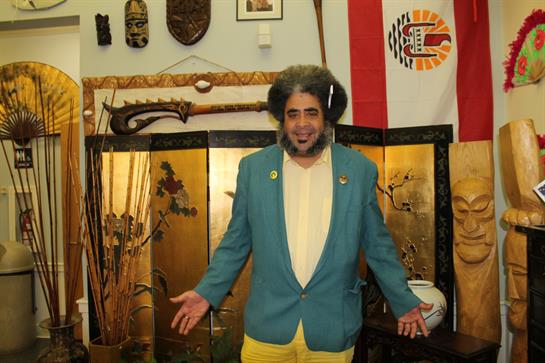 A man in a blue blazer and yellow pants joyfully invites guests into a vibrant, cultural space.