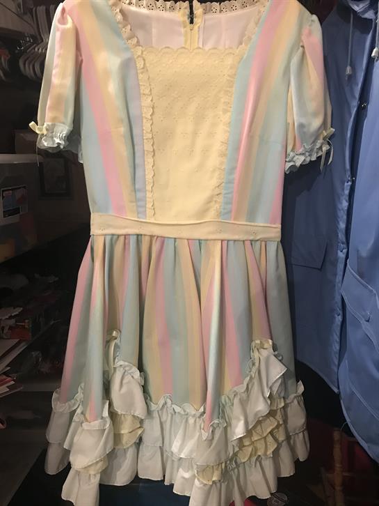 A vintage pastel dress with delicate ruffles hangs in a small clothing store.