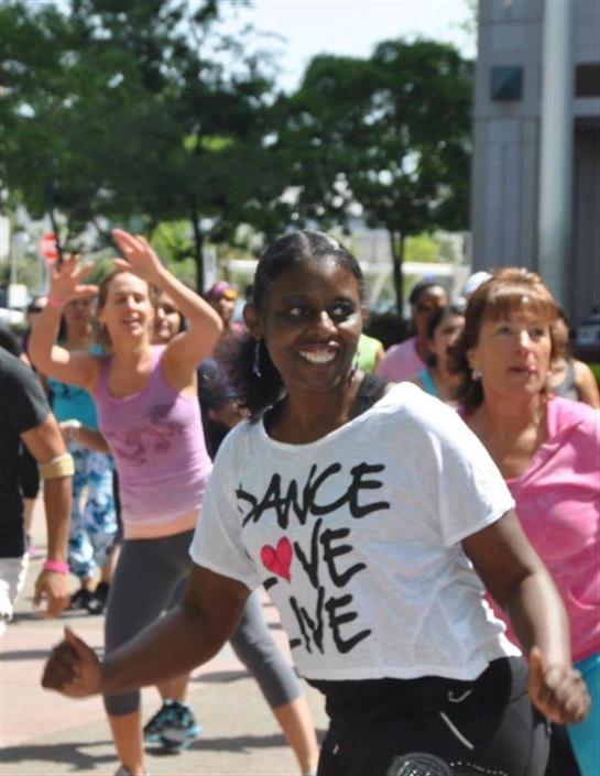 Participants engage joyfully in a dance class, showcasing movement and camaraderie under sunlight.