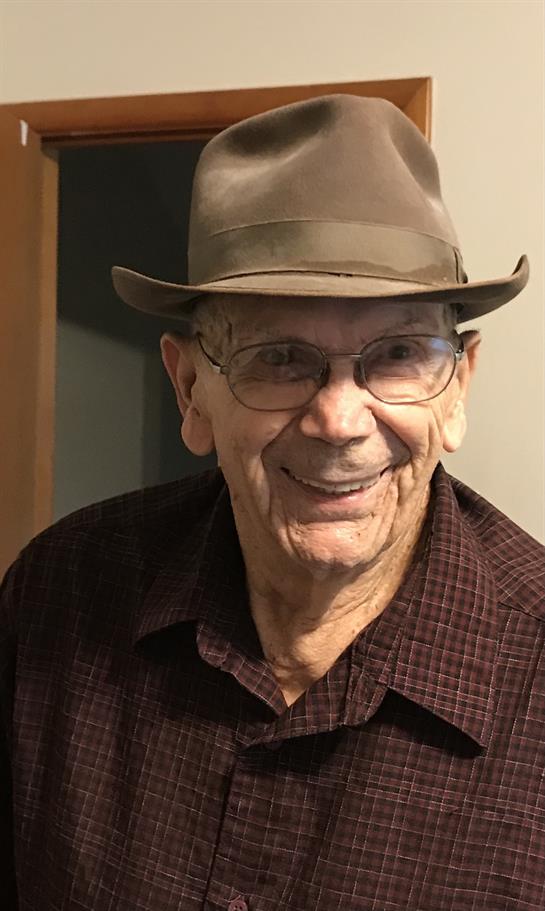 Elderly man with glasses and a hat smiles warmly while sitting indoors, radiating joy and warmth.