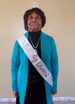 An older woman in a turquoise outfit and sash radiates joy on her special day.
