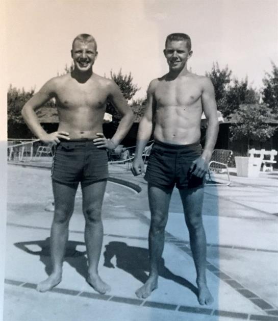 Two young men stand proudly at a pool, showcasing their summer tan and relaxed demeanor.