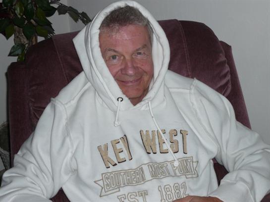 A smiling man in a white hoodie sits comfortably in a cozy chair, creating a relaxed vibe.