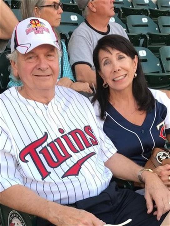 A happy couple sits together, wearing baseball jerseys, enjoying a game at a stadium.