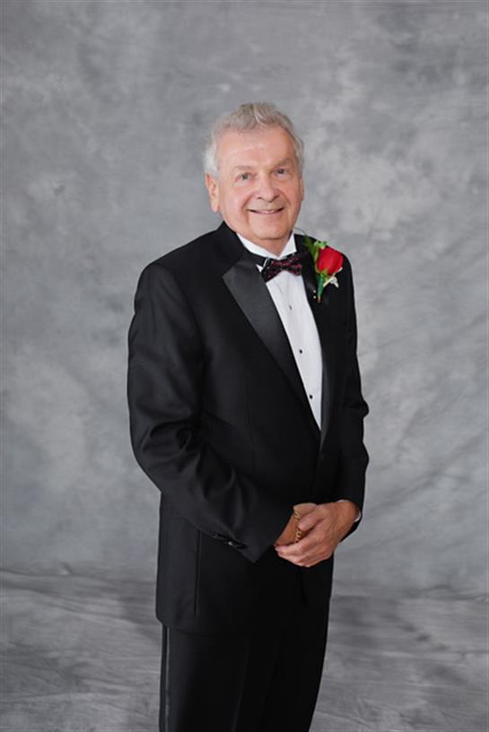 Senior man in a tuxedo with a rose stands confidently for a special event.
