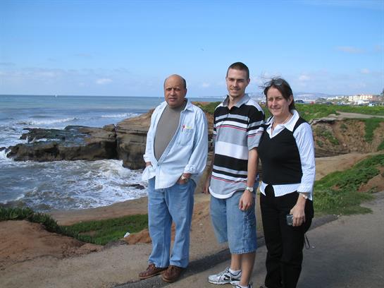 Three family members stand together by the ocean, enjoying a sunny day on the coast.