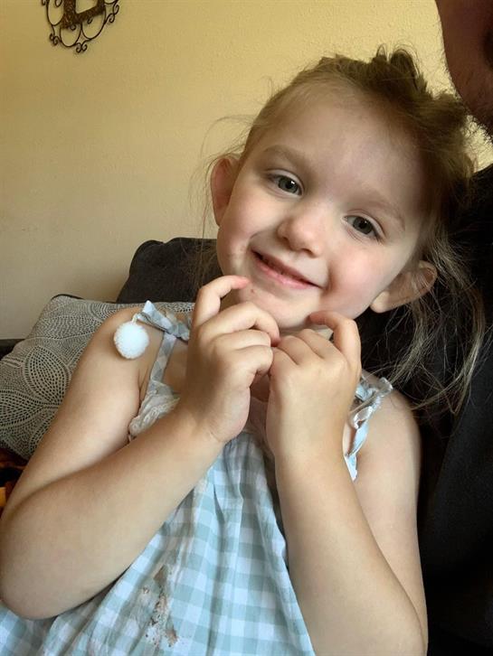 A young girl with a joyful expression sits indoors, enjoying a moment of playful happiness.