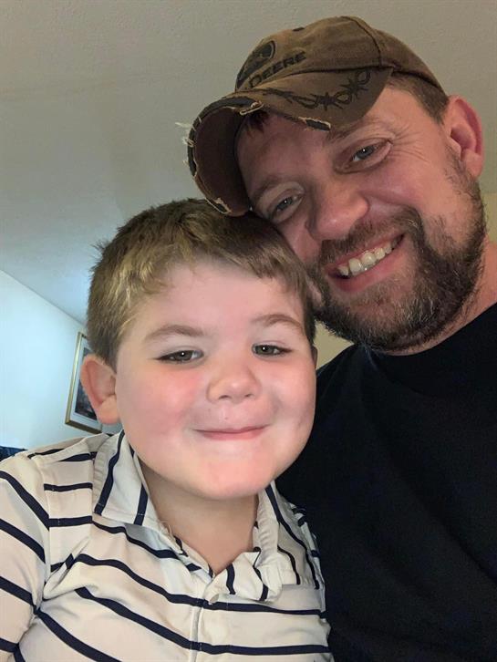 A father and his young son smile together, enjoying a cheerful moment at home in casual clothing.