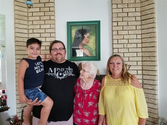 Four family members, including a child, gather with warm smiles in a home setting.