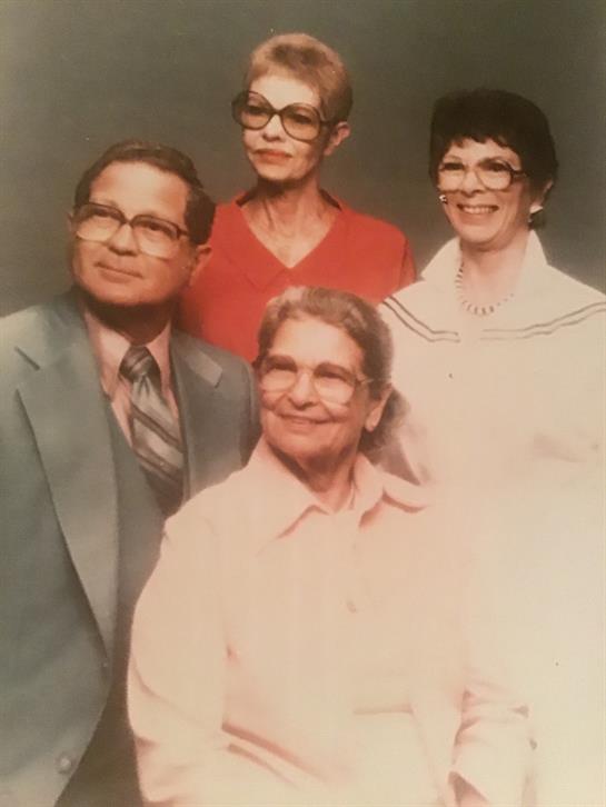 Four relatives are smiling and posing in a traditional studio setting with vintage clothing.