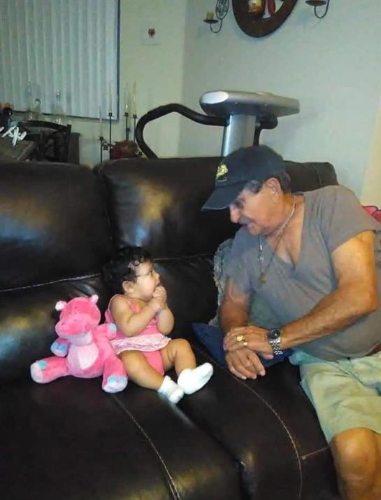 A grandfather interacts playfully with his granddaughter, who clutches a pink stuffed animal.