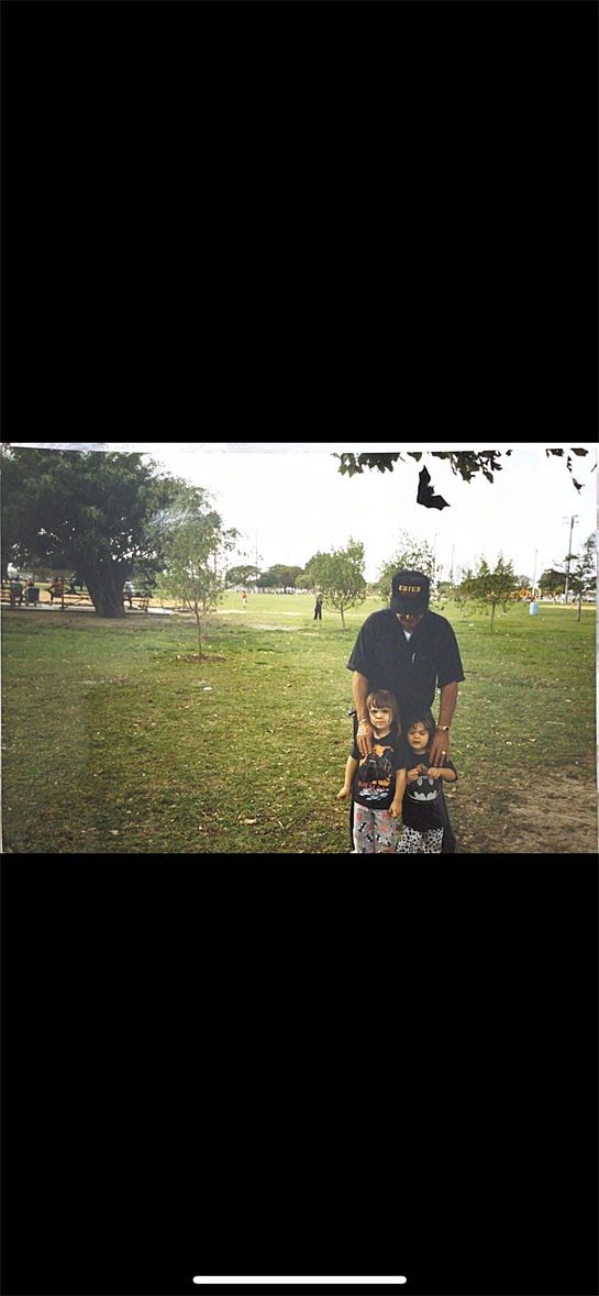 A father stands with his two children in a grassy park, sharing a joyful moment together.
