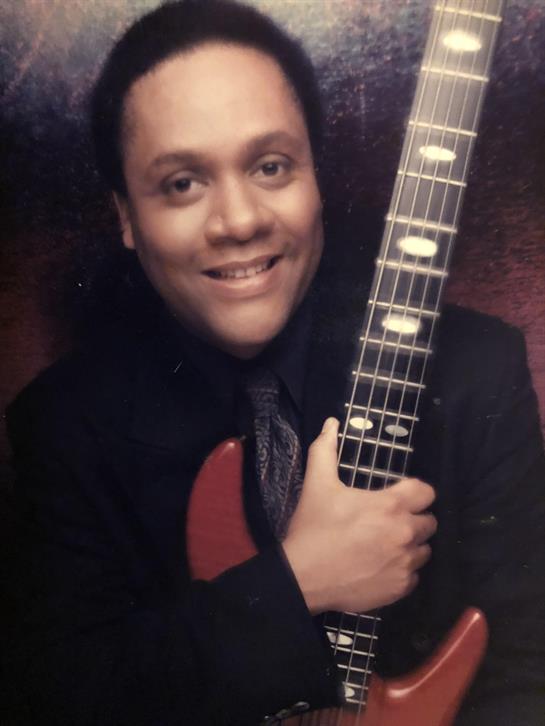 A joyful individual poses with a guitar, showcasing musical passion in a warm indoor setting.