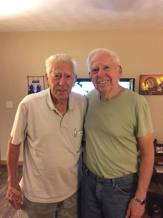 Two elderly men pose happily together indoors at a family gathering in a comfortable living room.