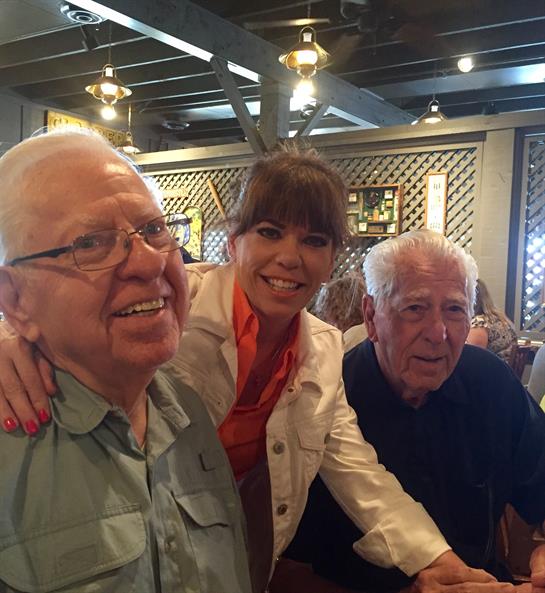 Three friends gather at a busy restaurant, sharing smiles and laughter in a cheerful atmosphere.