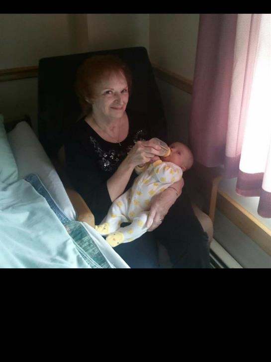 A woman smiles while holding and feeding a baby in a cozy, well-lit room.