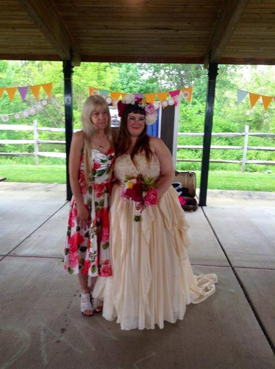Women pose joyfully in elegant dresses at a festive outdoor gathering surrounded by greenery.