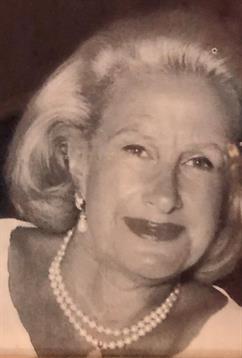 A smiling woman with light hair wears a pearl necklace while enjoying a party atmosphere.