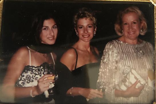 Three fashionable women enjoy an evening out, showcasing elegant attire and cheerful expressions.