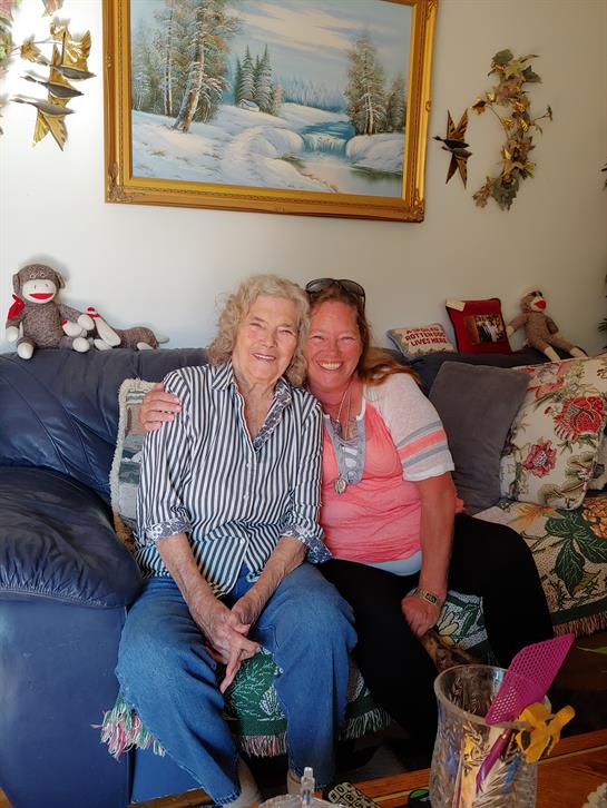 Two women smile together on a couch in a cozy, inviting living room.