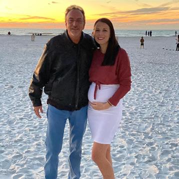 Man and woman pose together on the beach at sunset, enjoying a joyful moment by the ocean.