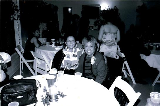 Two friends smile and pose together at a festive gathering with lively decorations around them.
