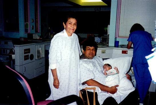 A family celebrates the arrival of a newborn in a hospital setting with warm smiles and affection.