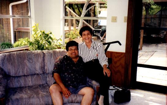 A couple relaxes on a couch in a bright living room, embracing and smiling at each other warmly.