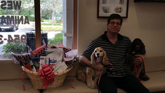 A man and his joyful dog pose together next to a large gift basket filled with presents.